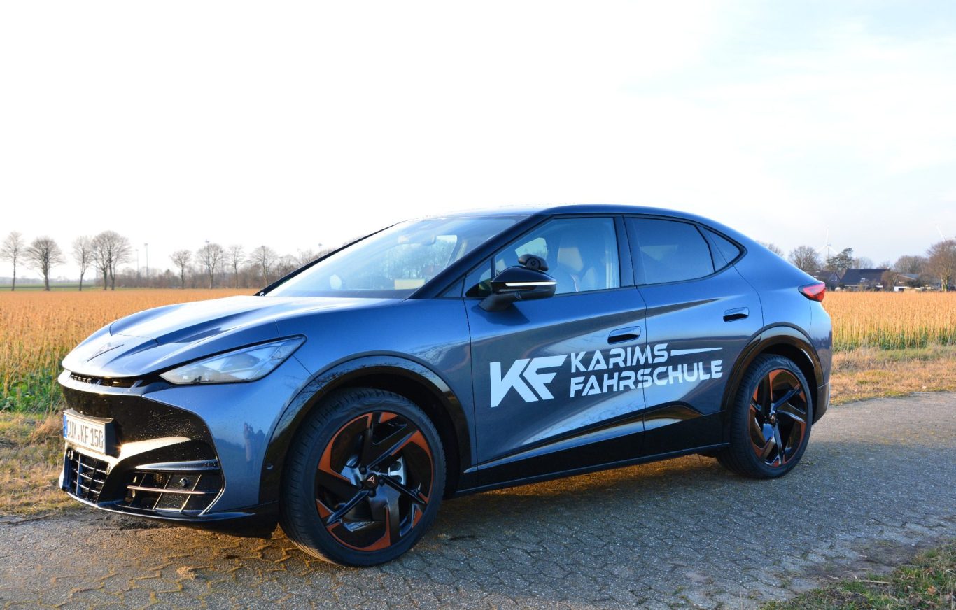 Sportliches Auto in blau mit kupferfarbenen Felgen, steht auf einem Feldweg im Sonnenuntergang.