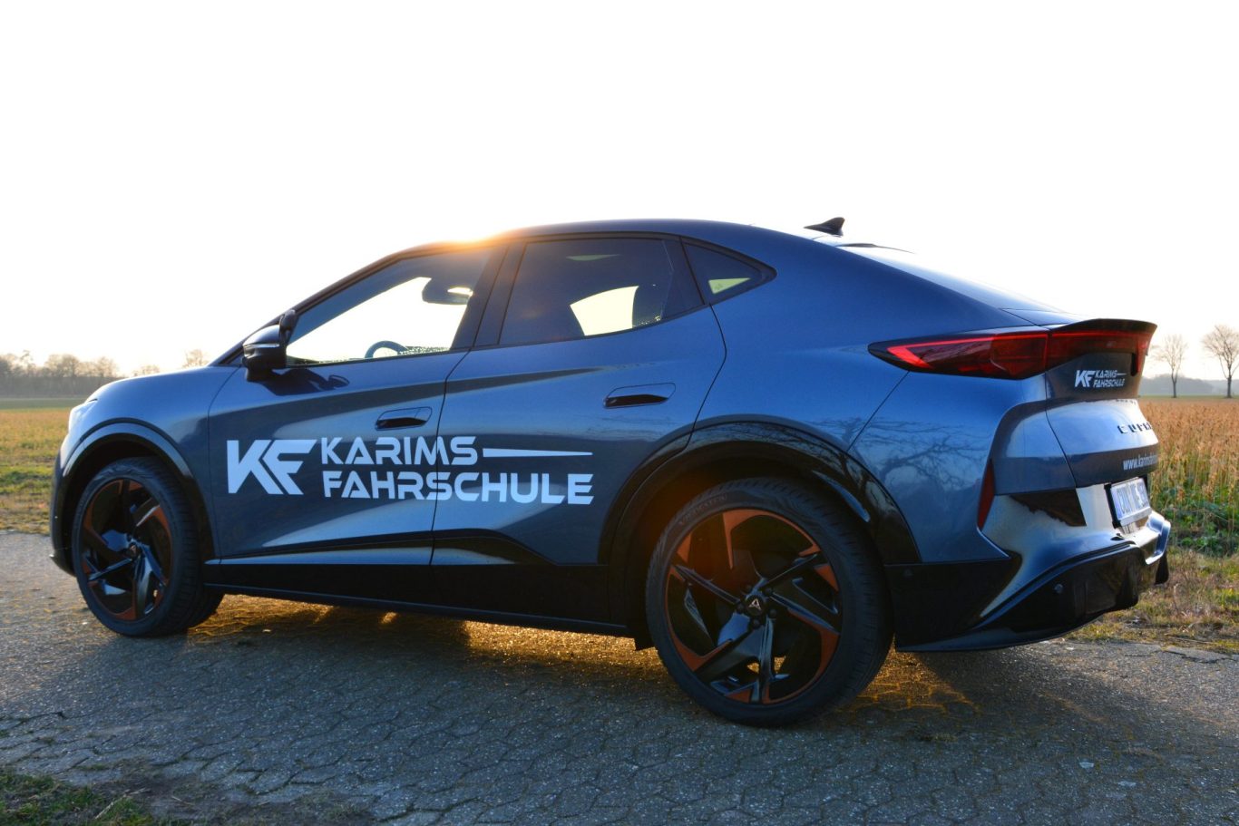 Dunkelblauer SUV mit Werbung auf der Seite, fährt auf einer Landstraße.