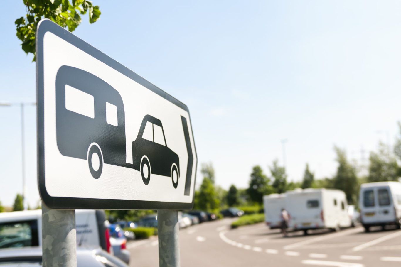 Verkehrszeichen für Anhänger und PKW, Parkplatz im Hintergrund.