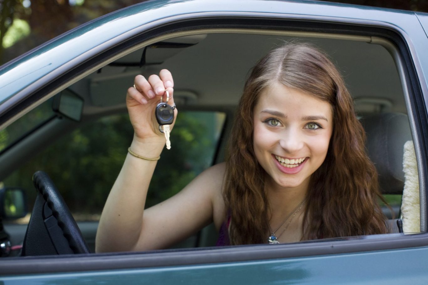 Junge Frau hält lächelnd einen Autoschlüssel aus dem Fenster eines Fahrzeugs.