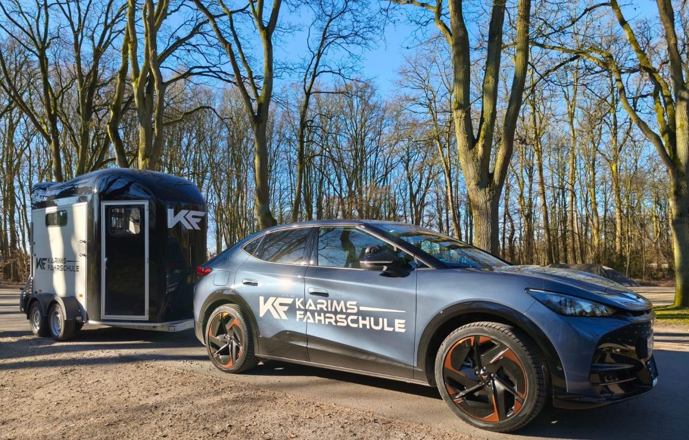 Ein SUV mit Pferdeanhänger, umgeben von Bäumen mit Sonnenschein