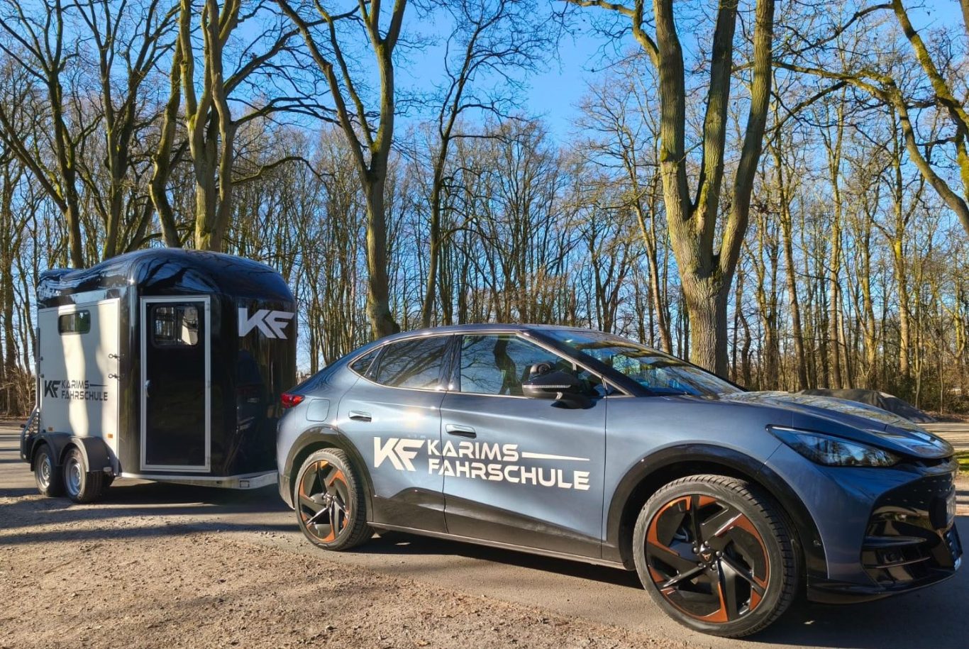 Dunkelblauer SUV mit Anhänger in einem Waldgebiet, klarem blauen Himmel.