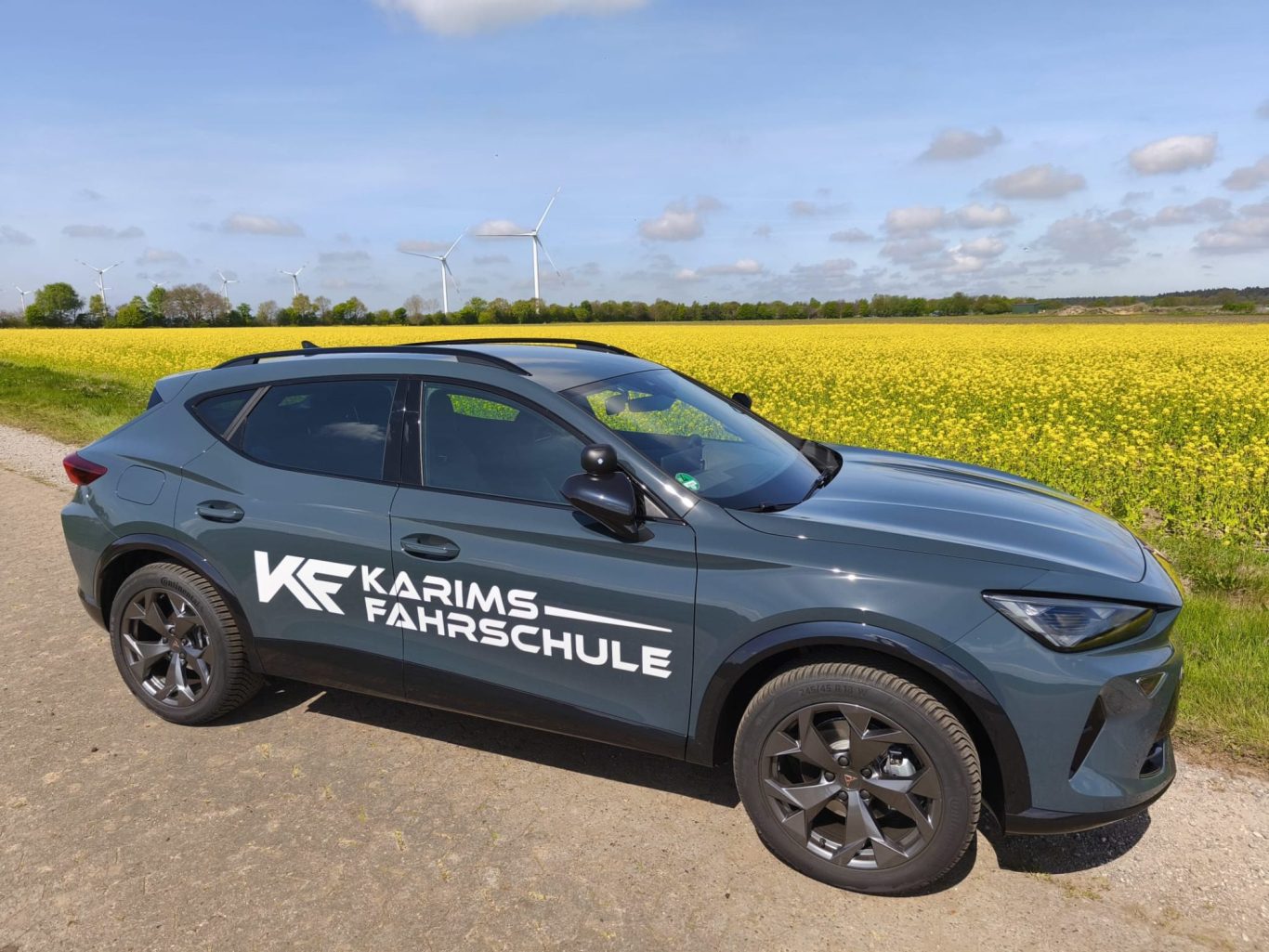 Ein grauer SUV mit einem Firmenlogo, umgeben von einem blühenden Rapsfeld.