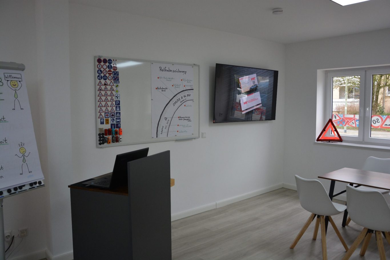 Helles Besprechungszimmer mit Whiteboard, Bildschirm und Tisch mit Stühlen.